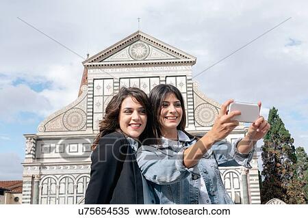 Stock Photography - Lesbian couple using smartphone to take selfie in front of church, Piazza Santa Maria Novella, Florence, Tuscany, Italy. Fotosearch