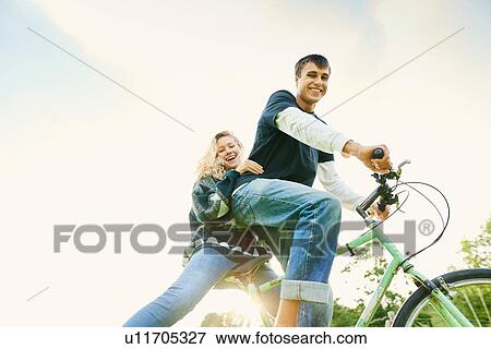 Low angle portrait of young couple on bicycle View Large Photo Image Stock Photo - Low angle portrait of young couple on bicycle. Fotosearch