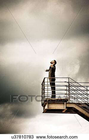 Stock Image - Low angle side view of mid adult man on stairs wearing suit, arms open thowing head back. Fotosearch