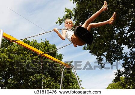 Stock Photograph - Low angle view of girl on swing looking at camera smiling. Fotosearch