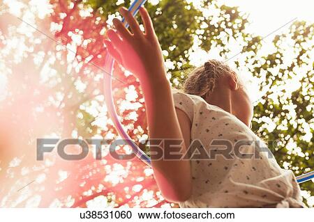 Stock Image - Low angle view of girl playing with hula hoop looking away. Fotosearch