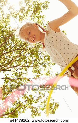 Low angle view of girl playing with hula hoop looking down smiling View Large Photo Image Stock Image - Low angle view of girl playing with hula hoop looking down smiling. Fotosearch