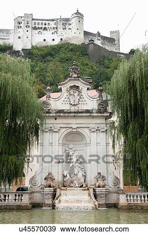 Stock Photo - Low angle view of Hohensalzburg Castle and Neptune fountain, Salzberg, Austria. Fotosearch