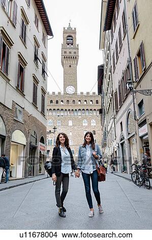 Picture - Low angle view of lesbian couple standing in street below the Palazzo Vecchio holding hands, Florence, Tuscany, Italy. Fotosearch