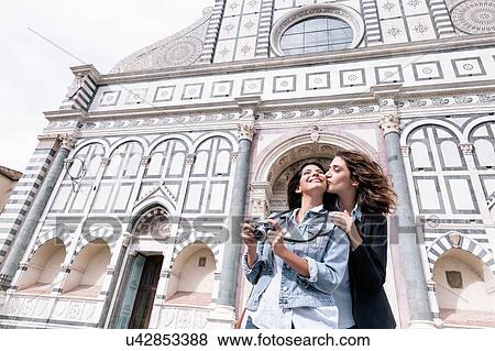 Low angle view of lesbian couple holding digital camera kissing on cheek in front of church, Piazza Santa Maria Novella, Florence, Tuscany, Italy View Large Photo Image Stock Photo - Low angle view of lesbian couple holding digital camera kissing on cheek in front of church, Piazza Santa Maria Novella, Florence, Tuscany, Italy. Fotosearch