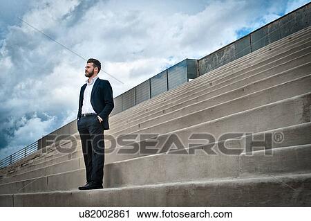 Low angle view of mid adult man on steps wearing suit, hands in pockets looking away View Large Photo Image Stock Image - Low angle view of mid adult man on steps wearing suit, hands in pockets looking away. Fotosearch
