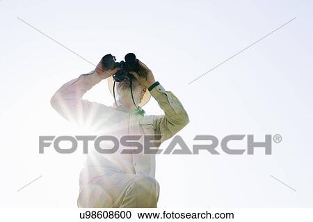 Stock Image - Low angle view of senior man in sunlight looking through binoculars. Fotosearch