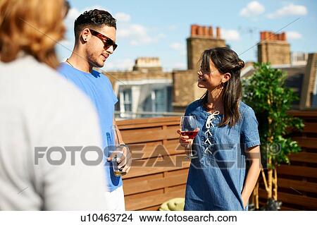 Picture - Male and female friends chatting and drinking at rooftop party. Fotosearch