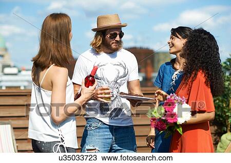 Stock Image - Male and female friends chatting at rooftop party. Fotosearch