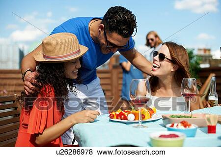 Stock Photo - Male and female friends chatting at rooftop barbecue. Fotosearch