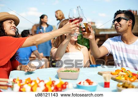 Stock Image - Male and female friends making a toast at rooftop barbecue. Fotosearch