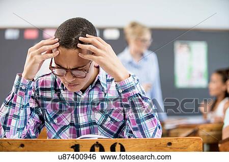 Stock Photograph - Male student, sitting at desk in classroom, looking confused. Fotosearch