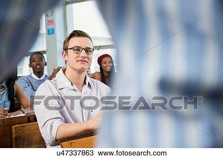 Stock Image - Male student sitting in classroon, listening to teacher. Fotosearch