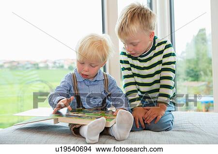 Picture - Male toddler and brother reading childrens book on sofa. Fotosearch