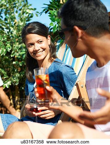 Man and woman sitting on deck chairs talking at rooftop party View Large Photo Image Stock Photo - Man and woman sitting on deck chairs talking at rooftop party. Fotosearch