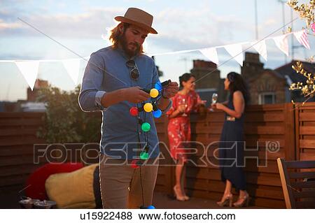 Stock Photo - Man hanging garden lights for early evening party. Fotosearch