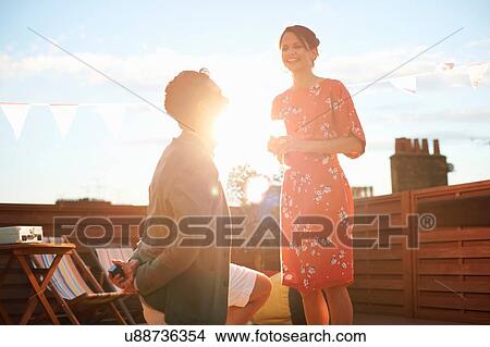 Picture - Man proposing to woman on roof terrace, sunset in background. Fotosearch