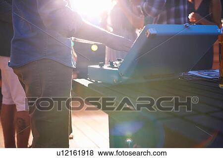 Stock Photo - Man putting on music at early evening party. Fotosearch