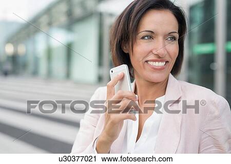 Stock Image - Mature businesswoman chatting on smartphone at airport. Fotosearch