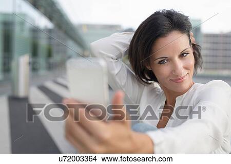 Mature businesswoman posing for smartphone selfie at airport View Large Photo Image Picture - Mature businesswoman posing for smartphone selfie at airport. Fotosearch