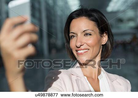 Mature businesswoman taking smartphone selfie at airport View Large Photo Image Stock Photo - Mature businesswoman taking smartphone selfie at airport. Fotosearch