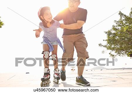 Stock Image - Mature man supporting daughter rollerblading at beach, Zhuhai, Guangdong, China. Fotosearch