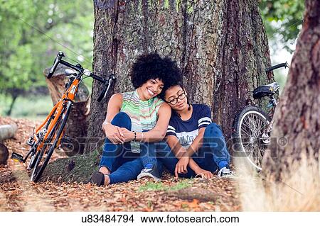 Picture - Mature woman and son sitting against park tree. Fotosearch