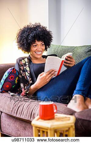 Stock Image - Mature woman relaxing on sofa reading book. Fotosearch