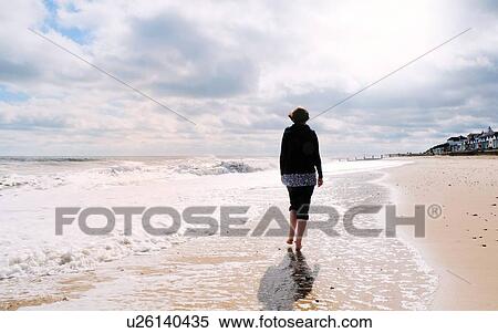 Stock Photography - Mature woman, walking along beach, rear view. Fotosearch