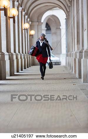 Mature woman with Christmas gift walking through city colonnade View Large Photo Image Stock Photo - Mature woman with Christmas gift walking through city colonnade. Fotosearch