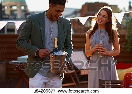 Mid adult couple at party on roof terrace holding ice bucket with champagne smiling View Large Photo Image Stock Photo - Mid adult couple at party on roof terrace holding ice bucket with champagne smiling. Fotosearch