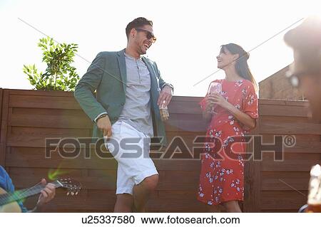 Stock Image - Mid adult couple chatting and drinking at rooftop party. Fotosearch