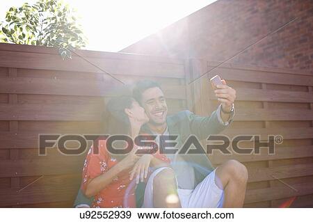 Stock Photo - Mid adult couple taking smartphone selfie at rooftop party. Fotosearch