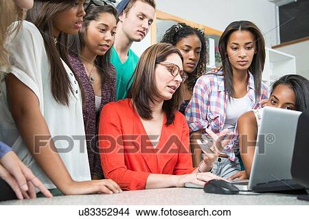Picture - Mid adult female teacher explaining on laptop to high school students. Fotosearch