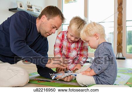 Stock Image - Mid adult man and two sons preparing toy airplane on living room floor. Fotosearch