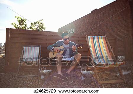 Mid adult man playing guitar on deckchair at rooftop party View Large Photo Image Stock Photo - Mid adult man playing guitar on deckchair at rooftop party. Fotosearch