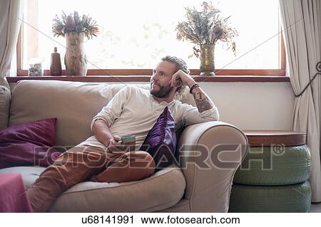 Mid adult man relaxing on sofa, drinking tea View Large Photo Image Stock Image - Mid adult man relaxing on sofa, drinking tea. Fotosearch