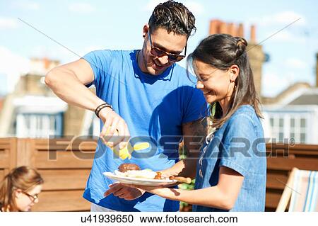 Mid adult man squirting mustard on burger at rooftop party View Large Photo Image Stock Image - Mid adult man squirting mustard on burger at rooftop party. Fotosearch