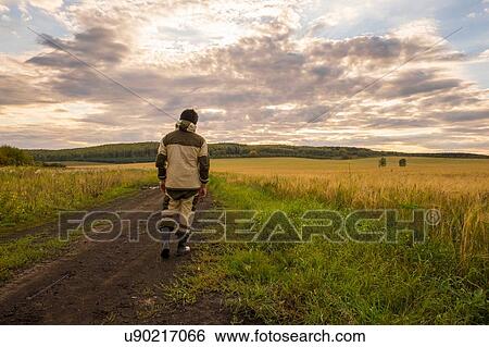 Stock Photograph - Mid adult man walking through field, rear view. Fotosearch