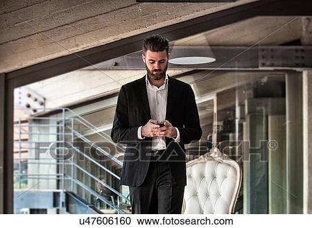 Mid adult man wearing suit holding smartphone looking down View Large Photo Image Stock Image - Mid adult man wearing suit holding smartphone looking down. Fotosearch