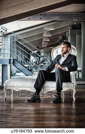 Mid adult man wearing suit sitting on chaise lounge looking away View Large Photo Image Stock Image - Mid adult man wearing suit sitting on chaise lounge looking away. Fotosearch
