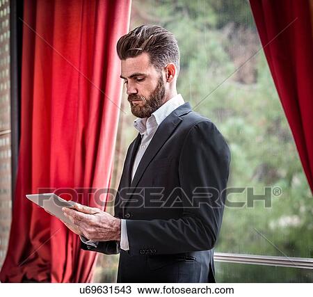 Mid adult man wearing suit standing in front window using digital tablet View Large Photo Image Stock Image - Mid adult man wearing suit standing in front window using digital tablet. Fotosearch