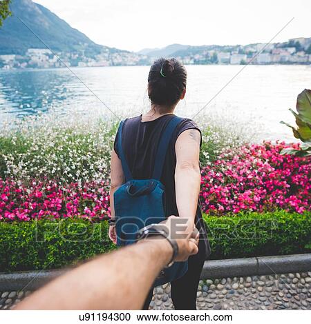 Stock Image - Mid adult tourist couple holding hands at Lake Lugano, Switzerland. Fotosearch