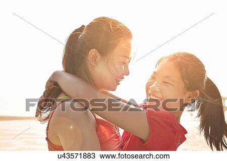 Stock Image - Mid adult woman and daughter hugging on beach, Zhuhai, Guangdong, China. Fotosearch
