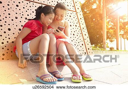 Picture - Mid adult woman and daughter reading smartphone texts, Zhuhai, Guangdong, China. Fotosearch