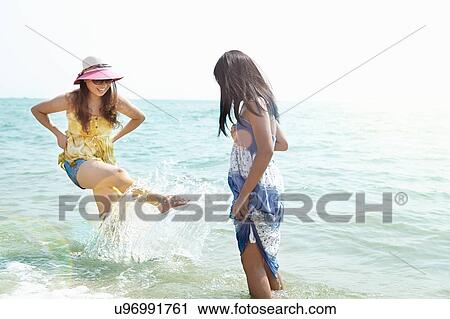 Stock Image - Mid adult woman and daughter splashing in sea, Zhuhai, Guangdong, China. Fotosearch