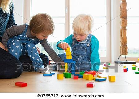Stock Image - Mid adult woman and two toddlers playing with building bricks on living room floor. Fotosearch