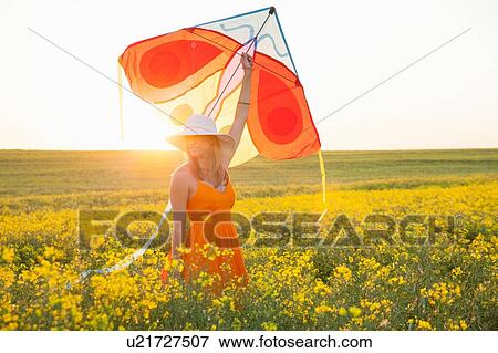 Mid adult woman in canola field arm raised holding kite View Large Photo Image Stock Photo - Mid adult woman in canola field arm raised holding kite. Fotosearch