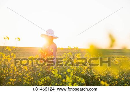 Mid adult woman in canola field wearing sunhat smiling, focus on background, lens flare View Large Photo Image Picture - Mid adult woman in canola field wearing sunhat smiling, focus on background, lens flare. Fotosearch