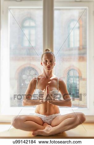 Picture - Mid adult woman in yoga position, in front of window. Fotosearch